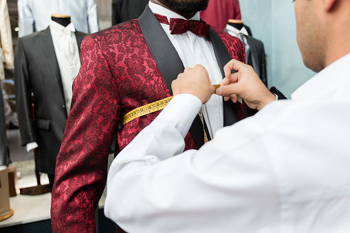 Detail of the hands of a tailor measuring  a tuxedo worn by an african-american man  at his shop