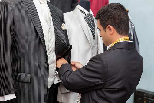 A tailor is checking the quality of a suit at his shop