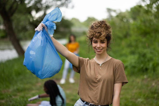 istock Smiling female volunteer standing in forest with garbage bag in hand while looking at camera 1336760399