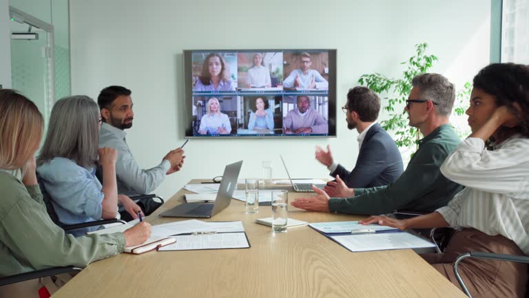 Diverse employees on online conference video call on tv screen in meeting room.