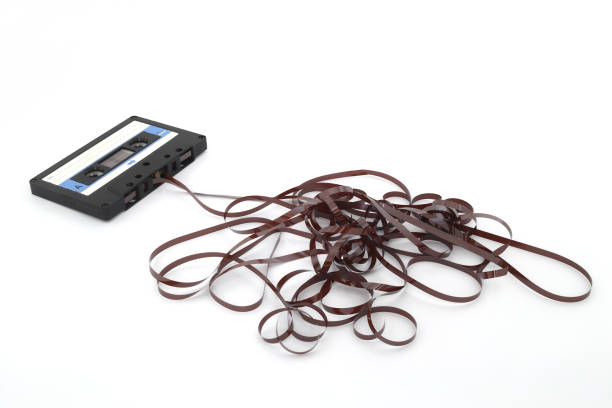 This shows a well known problem with the old fashioned compact cassettes: the tape used to come out, making the cassette useless. Vintage compact cassette tape on white background.