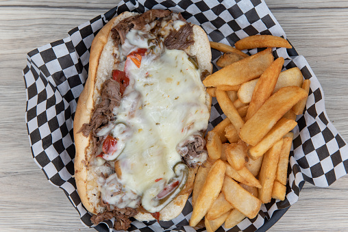 Overhead view of open faced Philly cheesesteak sandwich smothered in meled cheese served with steak french fries for an appetizing meal.