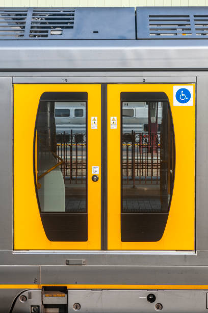 Modern double-deck (bi-level) electric commuter train with closed bright yellow entry doors with an older train in the background of a major city station.  Yellow is dominant colour: wheelchair accessible sign
