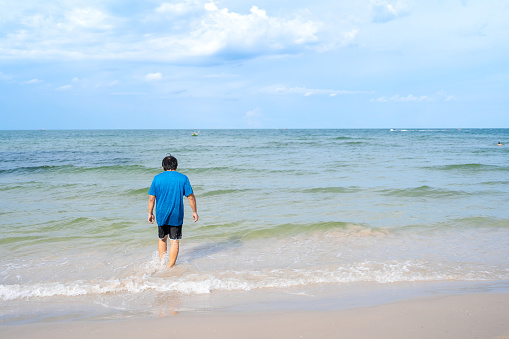 Asian man in the back in casual cloths walking into sea from beach, Huhin beach in Thailand, seascape view with blue sky