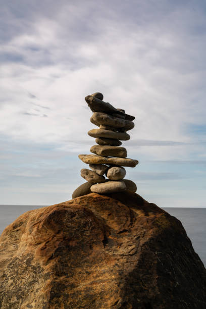 cairn rocheux méditatif au sommet d’un rocher avec une longue exposition à l’océan et au ciel en arrière-plan - long exposure rock cloud sky photos et images de collection