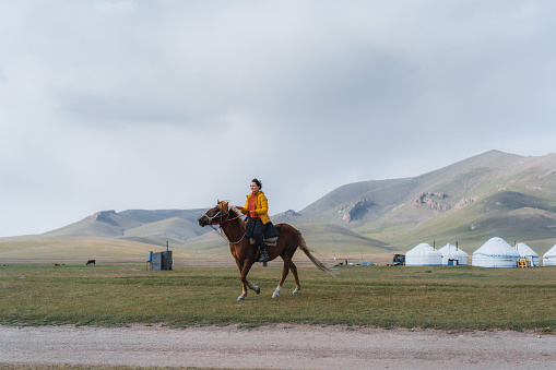 Young Caucasian woman riding on horse in mountains  of Kyrgyzstan on the background of yurts