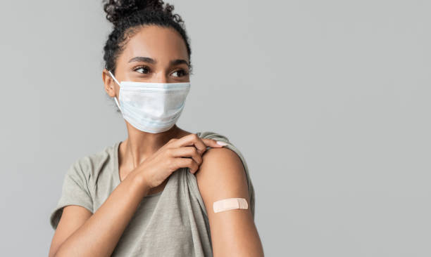 Portrait of a mixed race female girl wearing corona face mask after getting a vaccine. Woman showing her arm with bandage after receiving covid-19 vaccination. Corona virus protection, self care, healthy lifestyle concept. covid 19 vaccine stock pictures, royalty-free photos & images