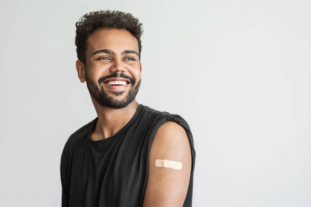 Man showing his vaccinated arm with plaster, got COVID-19 vaccine Young man received a corona vaccine looking away, isolated on gray background. Corona virus protection, self care, healthy lifestyle, vaccination concept. vaccination stock pictures, royalty-free photos & images