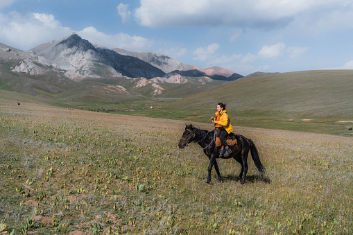 Young Caucasian woman riding on horse in mountains of Kyrygzstan