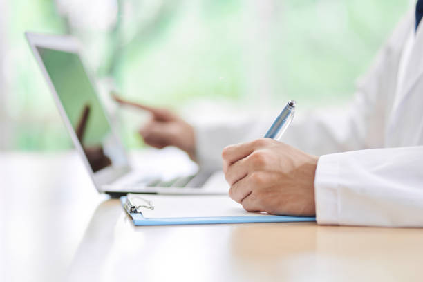 a male doctor who looks up on a computer and takes notes - research medical student doctor clinic imagens e fotografias de stock