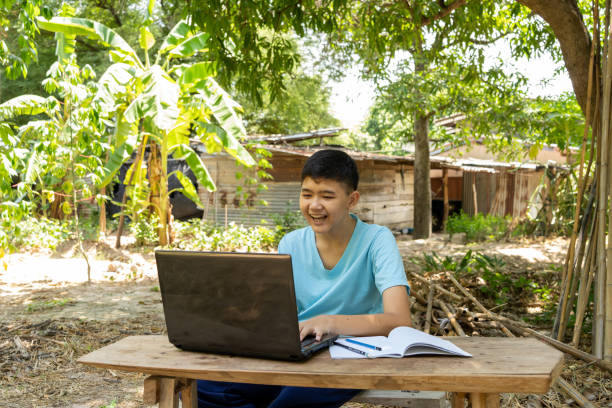 un ragazzo si diverte a studiare online con un computer portatile sulla sua scrivania a casa in campagna - asian country foto e immagini stock