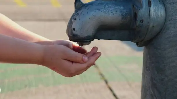 Photo of Caucasian Kid Cleaning Dirty Hands with Excessive Amount of Water Flowing from Public Tap Faucet Pump