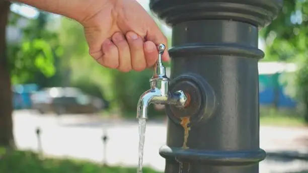 Photo of Caucasian Male Cooling and Cleaning His Hands with Fresh Water From Public Tap Fountain on Hot Summer Day