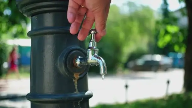 Photo of Caucasian Male Turning Off Water Dripping from Public Tap Faucet on Sunny Day