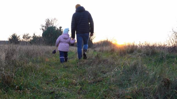 istock Kid and Parent Walking through High Grass Meadow during Sunset on Cold Autumn Day 1336836445