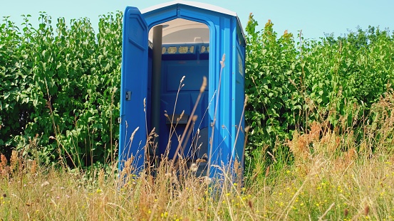 Blue Plastic Mobile Public Toilet Outhouse Standing in the Middle of High Grass Meadow During Open Air Music Festival