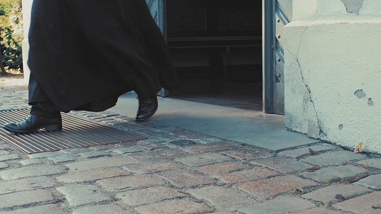 Sacerdote católico con sotanas negras saliendo de la puerta del vestíbulo de la iglesia photo