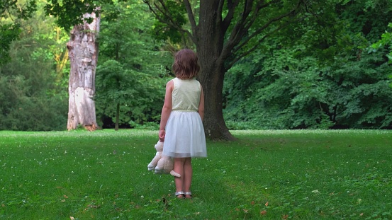 Cute curly toddler girl enjoying the nature while sitting on the meadow. Happy toddler girl sitting on a meadow with blooming cherry trees .