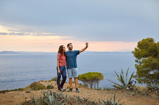 Man taking selfie with woman on cliff. Male and female camping during vacation. They are spending leisure time together.