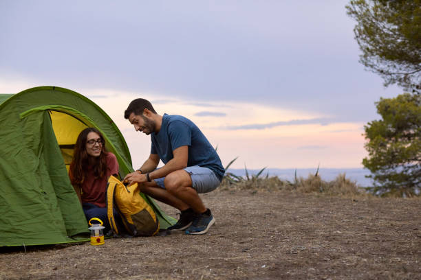 uśmiechnięta kobieta patrząca na mężczyznę otwierającego torbę przy namiocie - camping hiking tent couple zdjęcia i obrazy z banku zdjęć
