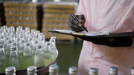 Mid section of a male worker holding clipboard and pen counting number of juice bottles in factory