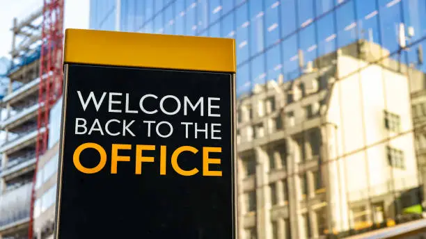 Welcome back to the office on a city-center sign in front of a modern office building