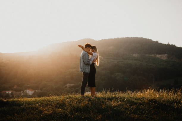 junges paar auf einem spaziergang in der natur bei sonnenuntergang auf dem land, umarmend. - küssen stock-fotos und bilder