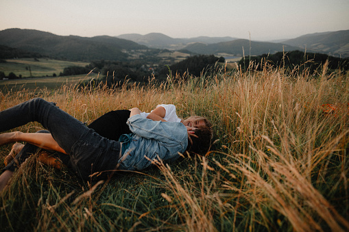 A young couple on a walk in nature in countryside, lying in grass having fun.