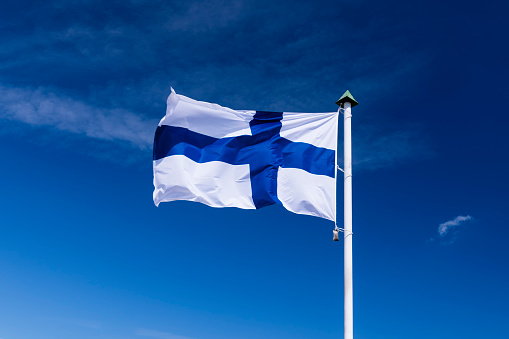 Finnish national flag waving on wind against blue cloudy sky