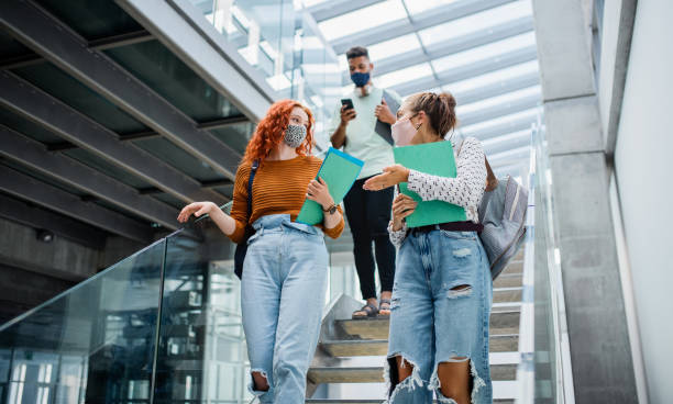 istock University students walking down and talking the stairs indoors, coronavirus concept. 1336859463