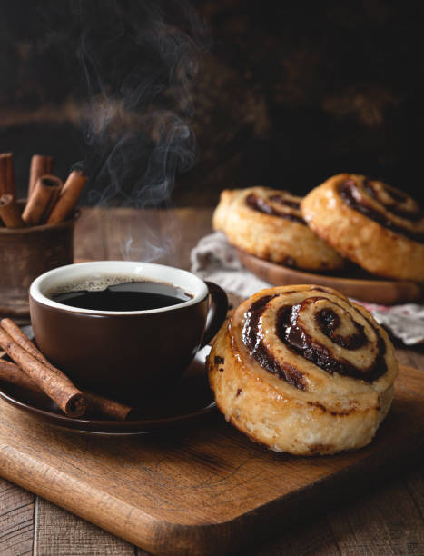 Cinnamon swirl roll and coffee Cinnamon roll and steaming hot cup of coffee with cinnamon sticks on a rustic wooden table sweet bun stock pictures, royalty-free photos & images