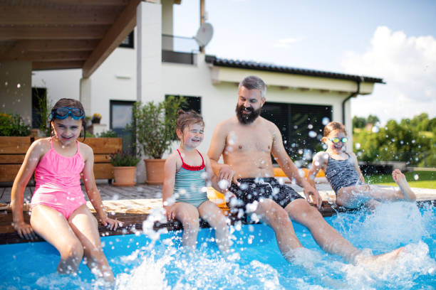 istock Father with three daughters outdoors in the backyard, sitting by swimming pool. 1336863729