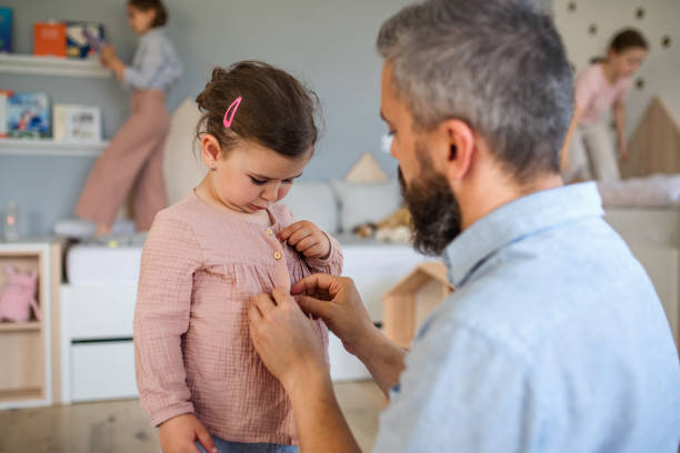 Father with three daughters indoors at home, helping to get dressed.