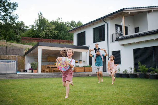 padre con tres hijas jugando al aire libre en el patio trasero, corriendo. - family houses fotografías e imágenes de stock