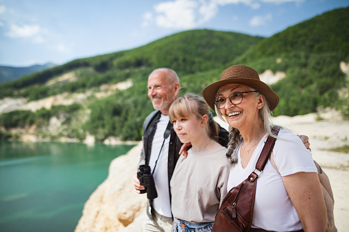 A happy preteen girl with grandparents on hiking trip on summer holiday, walking.