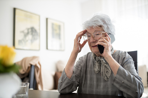 Sad and lonely senior gray-haired Caucasian woman talking on the mobile phone, receiving bad news. Loneliness and aging concept
