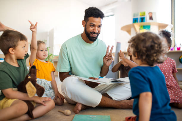 Group of small nursery school children with man teacher sitting on floor indoors in classroom, having lesson. A group of small nursery school children with man teacher sitting on floor indoors in classroom, having lesson. preschool classroom jobs stock pictures, royalty-free photos & images