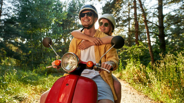 Smiling young caucasian friends riding scooter in wood stock photo