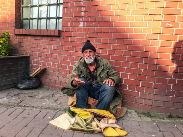 Dishevelled and dirty homeless man in a town centre. Posed by model.