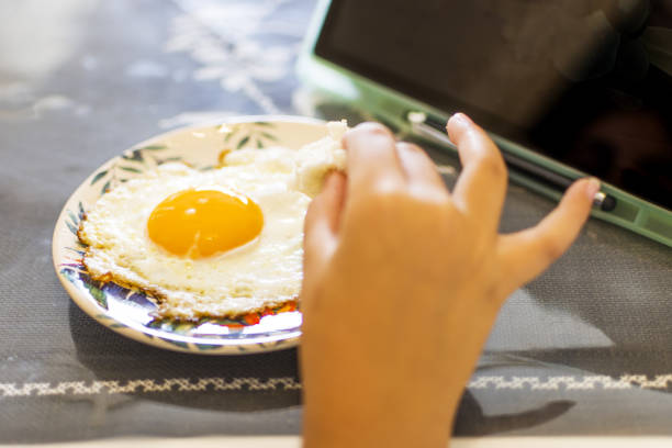 istock Little girl eating perfect fried egg, using digital tablet 1336887094