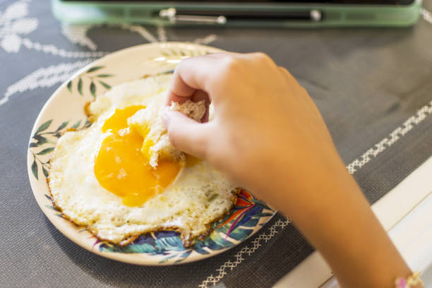 istock Little girl eating perfect fried egg, using digital tablet 1336888435