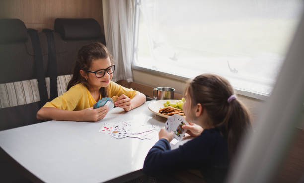 Small girls playing cards indoors in caravan, family holiday trip. Happy small girls playing cards indoors in caravan, family holiday trip. family playing card game stock pictures, royalty-free photos & images