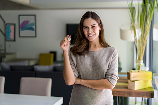 Portrait of a pregnant Latin American woman holding the keys to her new house and looking at the camera smiling
