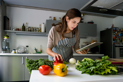Latin American woman cooking at home following an online recipe on her tablet - lifestyle concepts