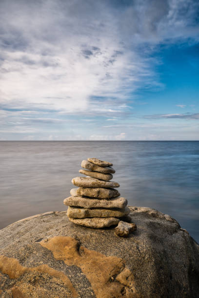 cairn rocheux méditatif au sommet d’un rocher avec une longue exposition à l’océan et au ciel en arrière-plan - long exposure rock cloud sky photos et images de collection