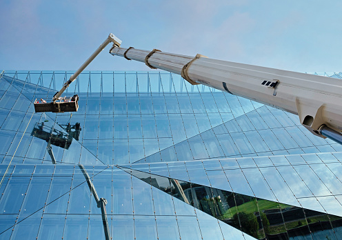 Maintenance works being done on a building. Workers are cleaning windows from a boom lift, Aerial work platform, aerial device, elevating work platform.