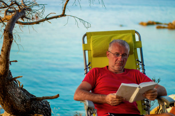 istock Man is reading a book next to the see 1336907282