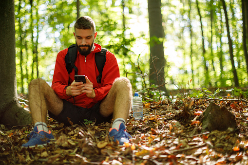 Young man using mobile phone and relaxing in forest