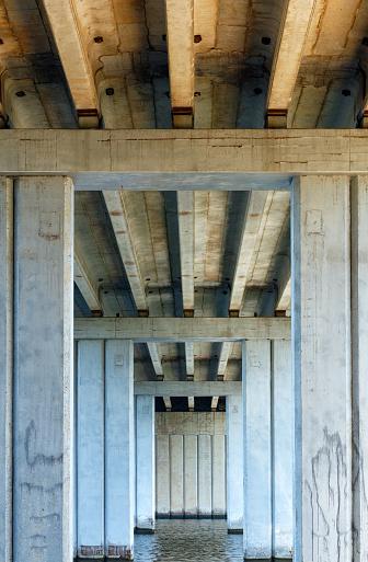 Bottom view of symmetrical concrete truss structures, concrete beams and pillars of the bridge that crosses the river and supports the six-lane expressway. Vertical image, copy space.