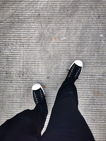 Photo of human foot with black jeans and black shoes with line pattern background